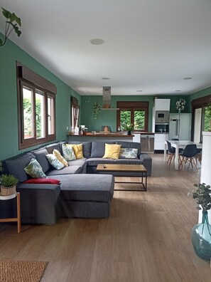 A modern kitchen with a dining area, a grey sectional sofa, and a wooden coffee table.