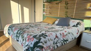 A bedroom with a bed, a nightstand, a wooden headboard, and a window with blinds.