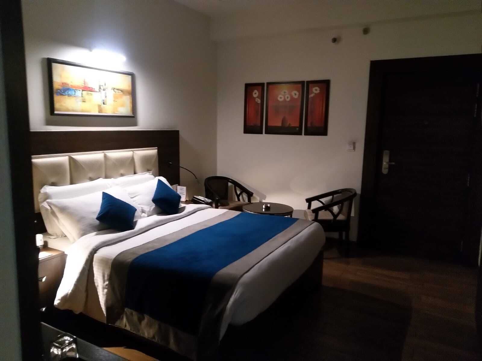 A hotel room with a bed, a desk, two chairs, and artwork on the walls.