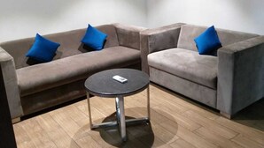 A corner seating area with two sofas and a small round table, a ceiling-mounted air conditioner, and wooden flooring. - JB SKY HILTON INN (Lucknow)