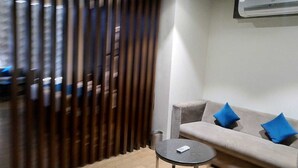 A modern living room with a sofa, a round table, and a decorative wooden partition. - JB SKY HILTON INN (Lucknow)