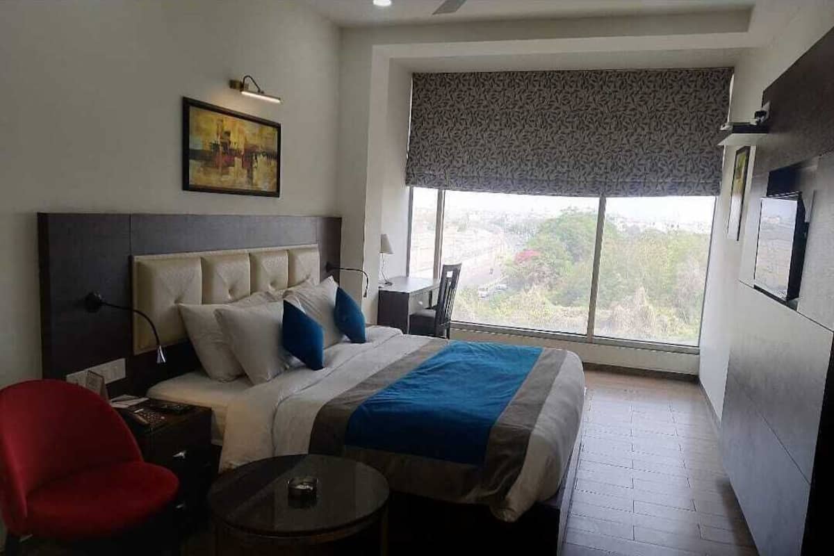 Habitación de hotel con una cama grande, un escritorio, una silla, una mesita y una ventana con vistas.
