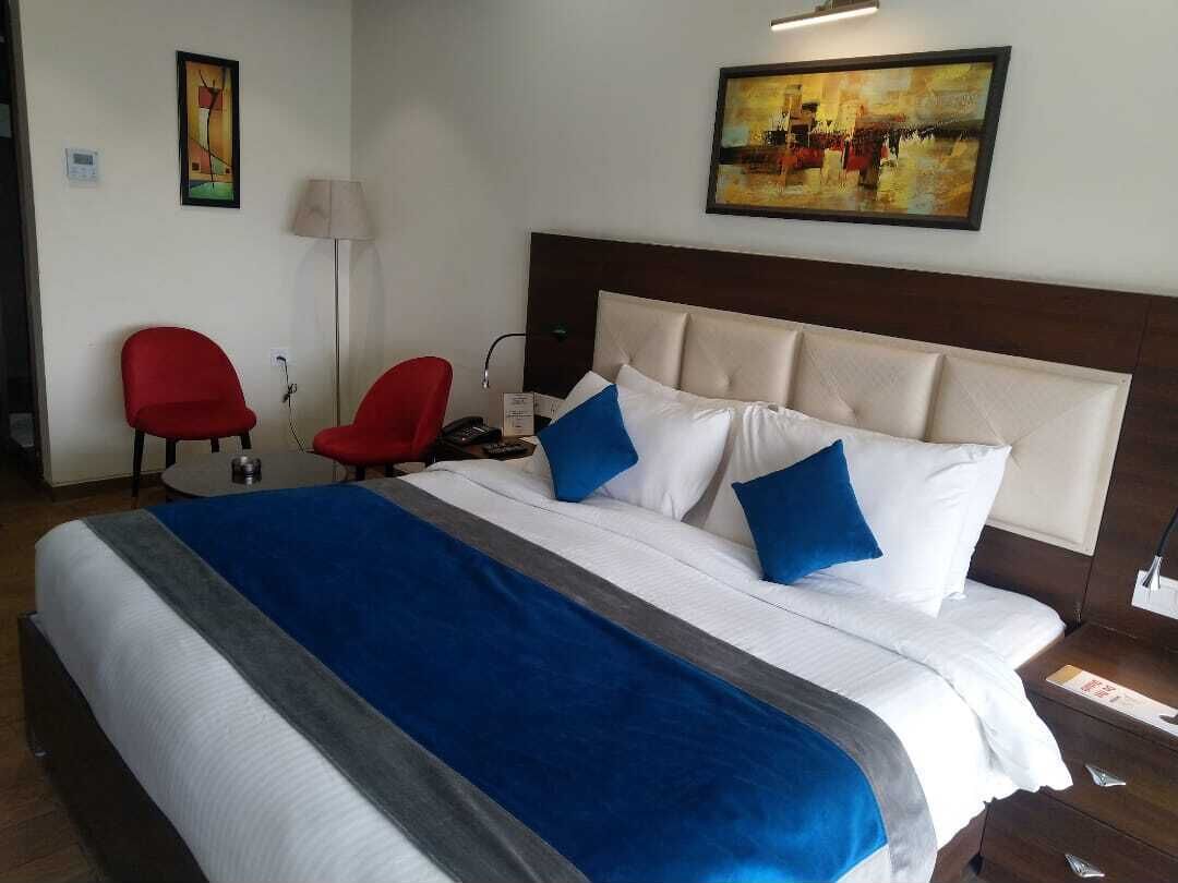 A hotel room with a large bed, two red chairs, a desk, a lamp, and artwork on the walls.