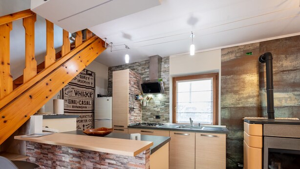 Una cocina moderna con una isla central, una escalera de madera y un estufa de leña integrada.