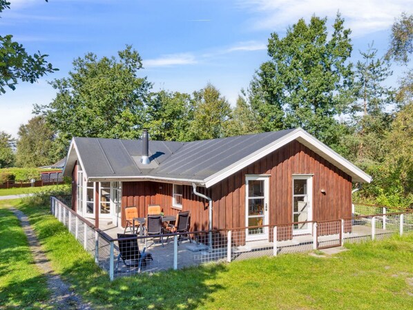 A wooden cabin with a covered patio, a chimney, and a fenced outdoor area.