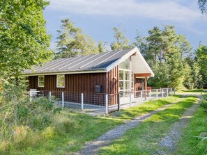 A wooden cabin with a metal roof, a fenced porch, and a gravel path leading to it.