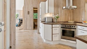A modern kitchen with wooden paneling, white cabinetry, a stainless steel range hood, and a built-in oven. - "Telse" - 200m from the sea by Interhome (Grenaa)