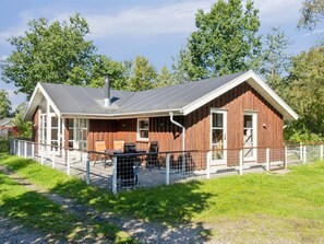 A wooden cabin with a covered patio area, a chimney, and a fenced outdoor seating area.