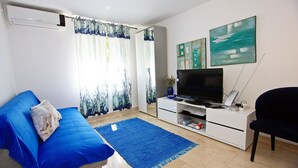 Ett vardagsrum med en blå soffa, en tv-apparat på ett vitt skåp och konstverk på väggen.