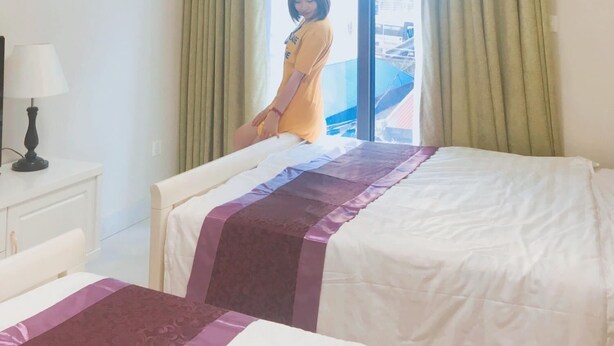 Una habitación de hotel con cama, mesita de noche, lámpara y ventana con cortinas.