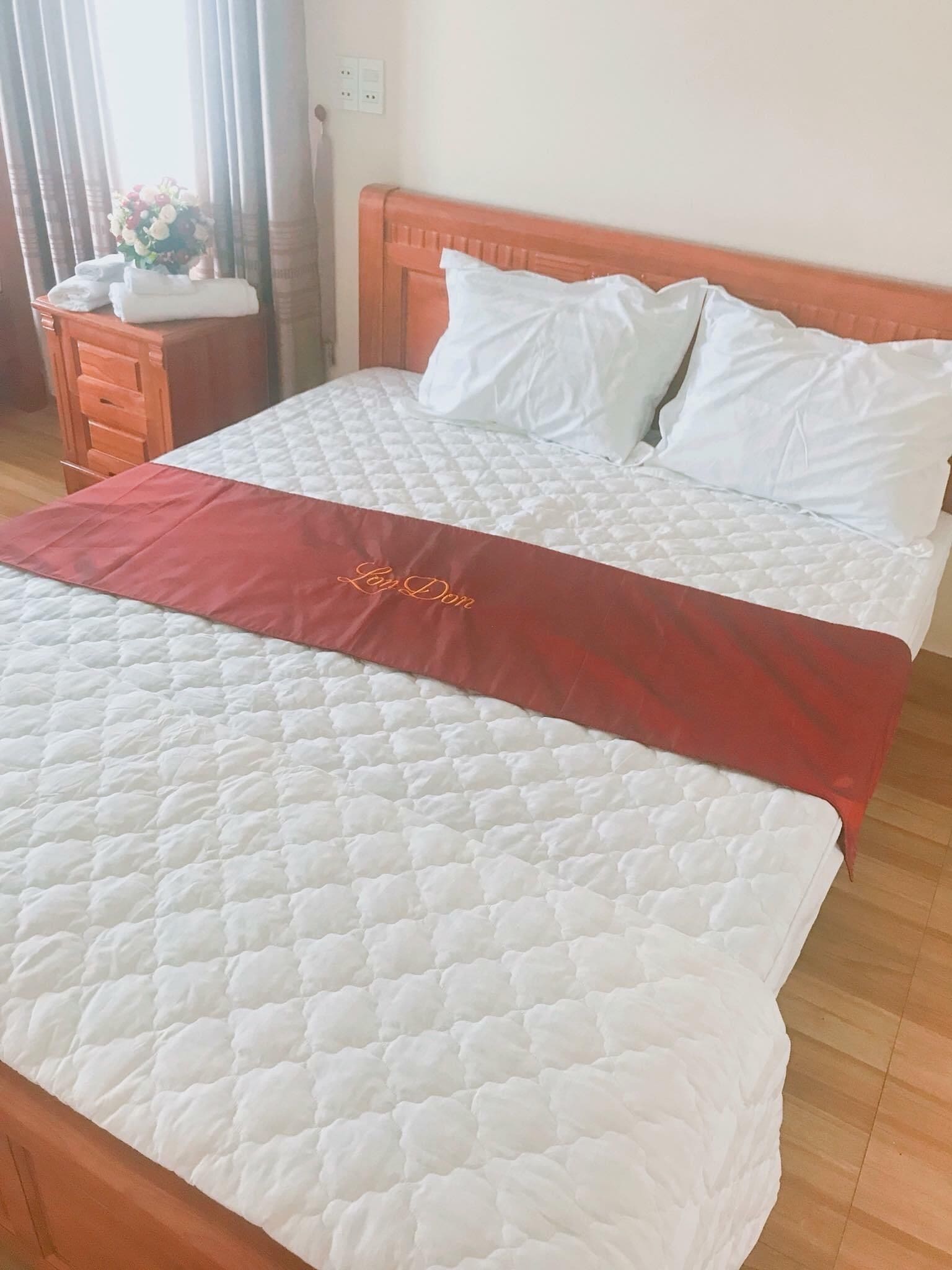 A neatly made bed with a red bed runner, white pillows, and a wooden headboard.