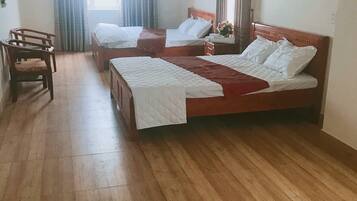 Een hotelkamer met twee bedden, een houten vloer, een bureau met stoel en een raam met gordijnen.