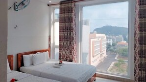 Habitación de hotel con dos camas, un ventanal con cortinas, un ventilador de techo y vistas a edificios y colinas.