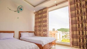 Un dormitorio con dos camas de madera, un ventanal con cortinas estampadas y un ventilador de pared.