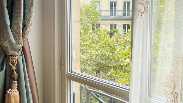 A window with curtains, a view of a building, and a balcony railing.