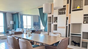 A modern living room with a wooden dining table, four chairs, a sofa, and a bookshelf.