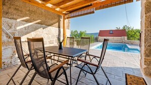 An outdoor patio with a table and chairs, a stone wall, and a view of a swimming pool and house. - Holiday Home Rustic - Two Bedroom Holiday Home with Private Pool (Crivac)