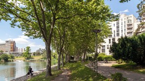 A park with a path, trees, a body of water, and a building in the background.