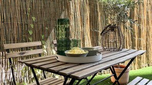 An outdoor patio with a table set for dining, surrounded by a bamboo fence and a green lawn.
