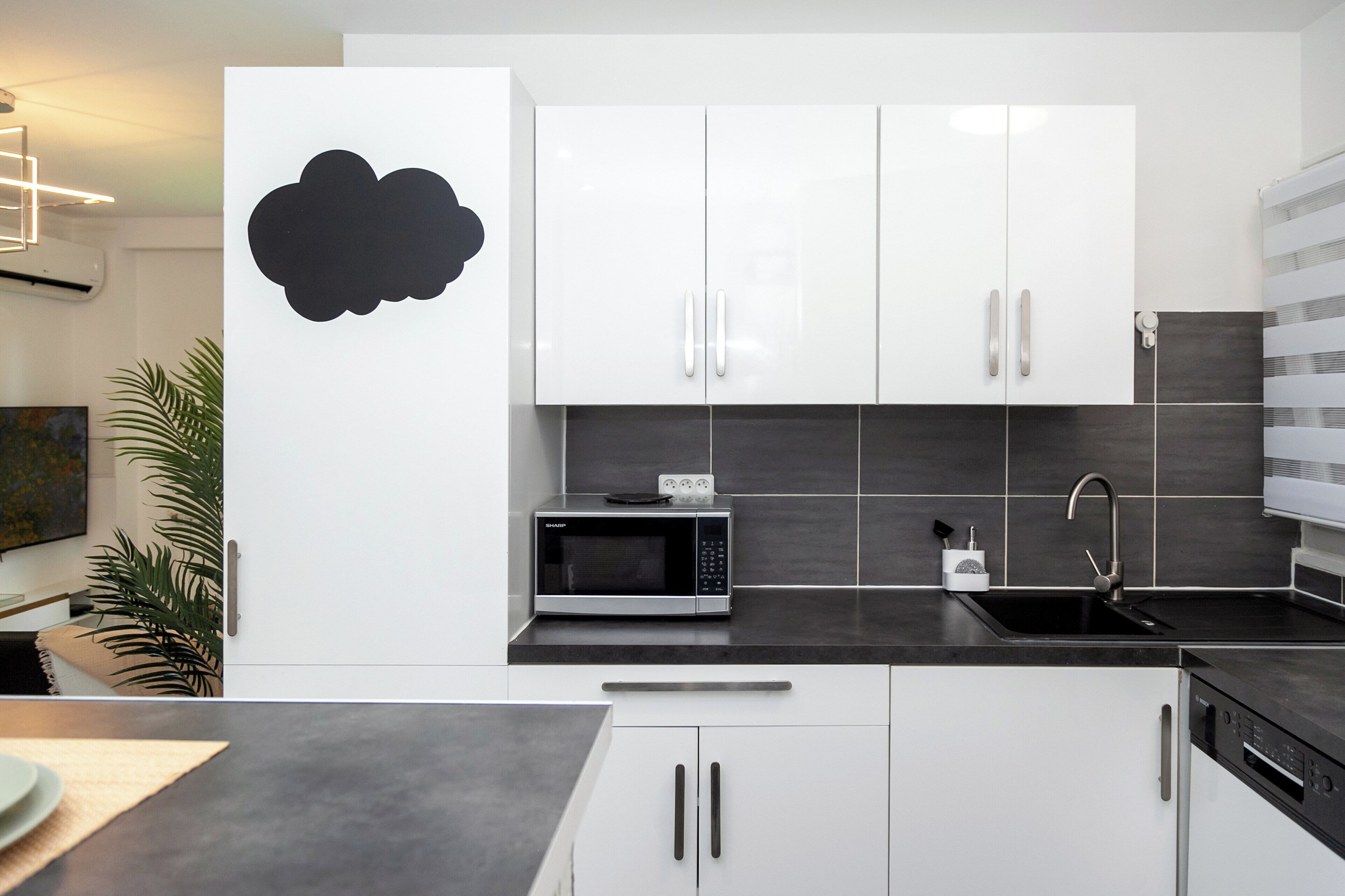 A modern kitchen with white cabinets, a microwave, a sink, and a dishwasher.
