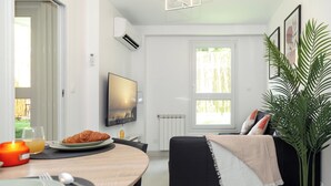 A modern living room with a dining area, a black sofa, a potted plant, and a television.