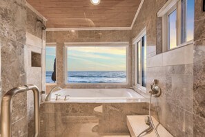 A bathroom with a large bathtub, a shower, and a view of the ocean through a window.