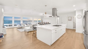 A modern kitchen with a large island, white cabinetry, and a view of the ocean through large windows. - @Marbella Lane-Oceanfront Retreat w/ Stunning View (Pacifica)