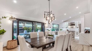 A modern kitchen with white cabinets, a central island, and a dining area with a wooden table and white chairs. - The Kensington| Luxe 4BR | Pool | Al-Fresco Living (Scottsdale)