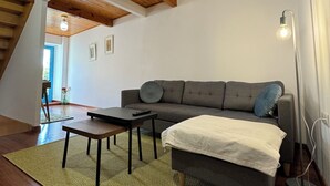 A cozy loft bedroom with a wooden ceiling, a gray sofa, a small table, and a floor lamp.