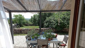 An outdoor patio with a table and chairs, surrounded by gravel, under a shaded pergola. - Apartment with garden and pool near fabulous sights (Rocamadour)
