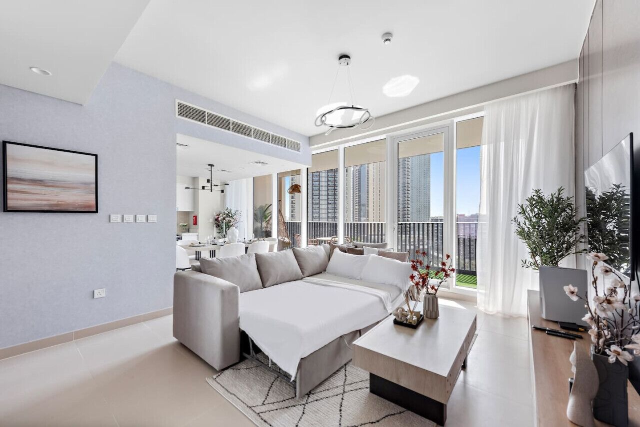 A modern living room with a sectional sofa, a coffee table, and a large window offering a city view.