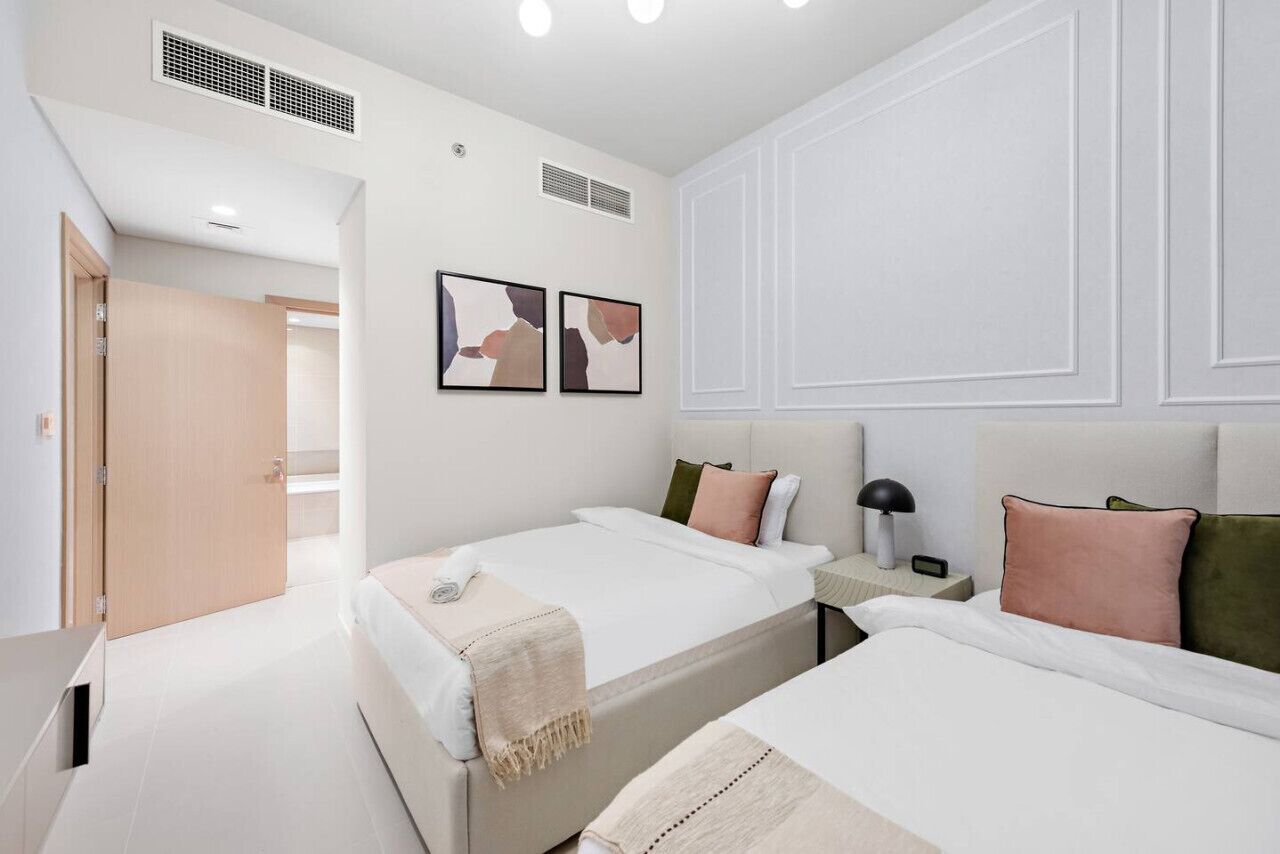 Una habitación de hotel moderna con dos camas, una mesita de noche con lámpara y una obra de arte en la pared.