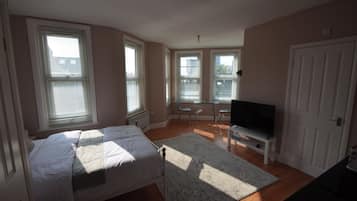 A bedroom with a bed, a TV on a stand, and a desk with a chair.