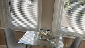 Un coin repas avec une table en verre et deux chaises grises, une petite plante en pot et un flacon de gel hydroalcoolique.