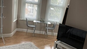 Une pièce comprenant une table à manger et des chaises, un téléviseur posé sur un meuble, une lampe sur pied et un tapis à motifs.