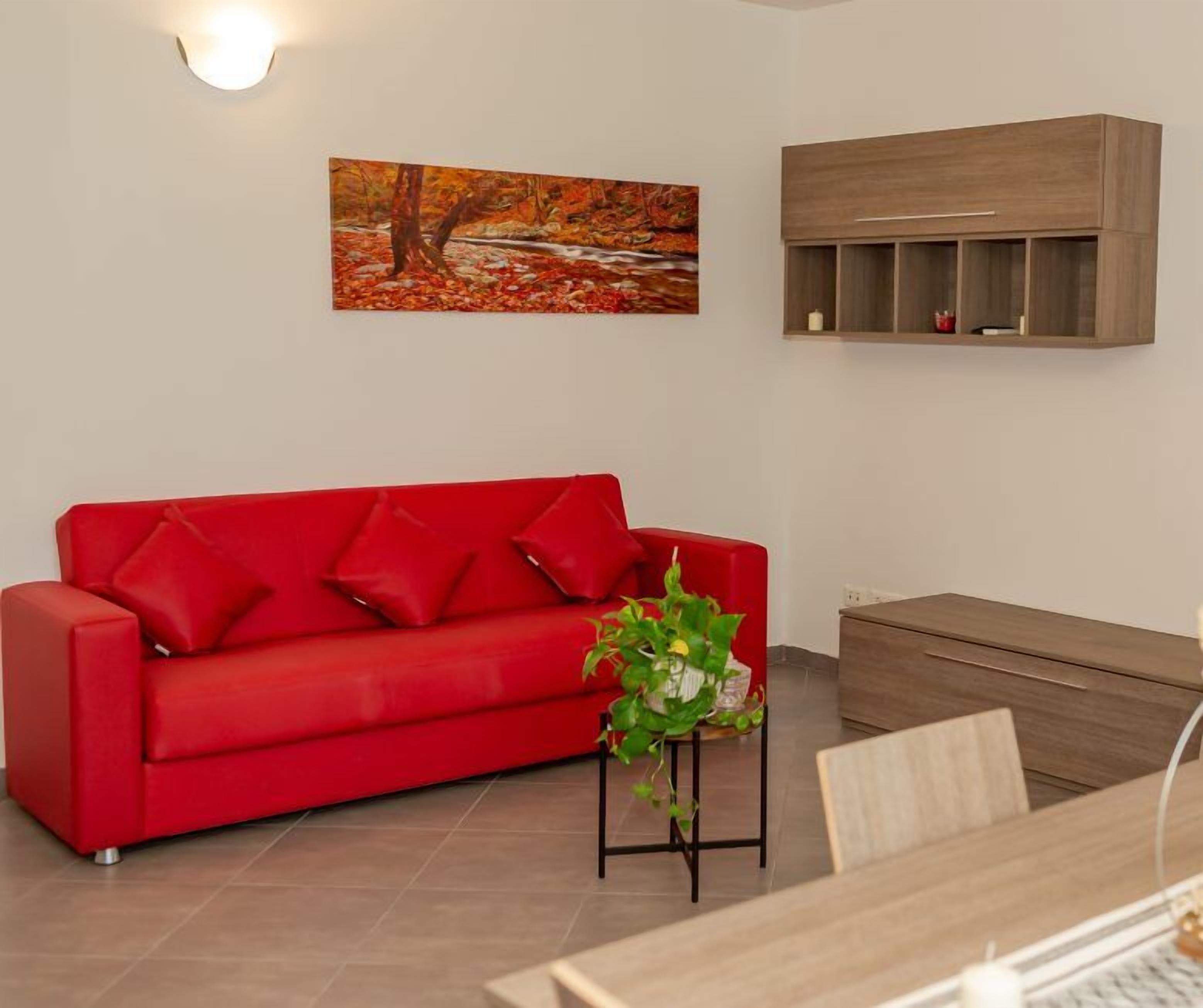 A red sofa with matching cushions, a small table with a potted plant, and a wooden cabinet against a white wall.