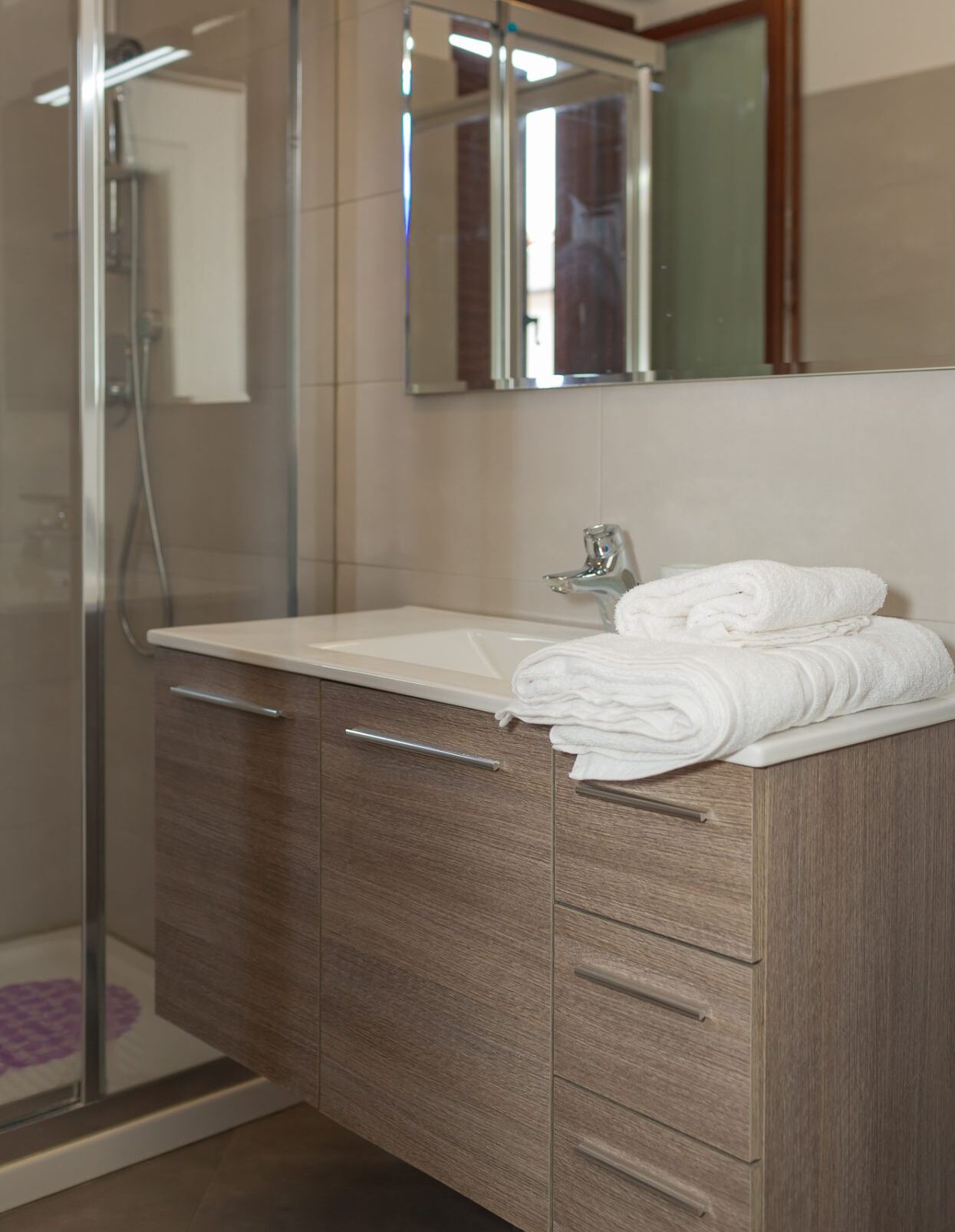 A modern bathroom with a glass shower enclosure, a white sink, and a wooden vanity with drawers.