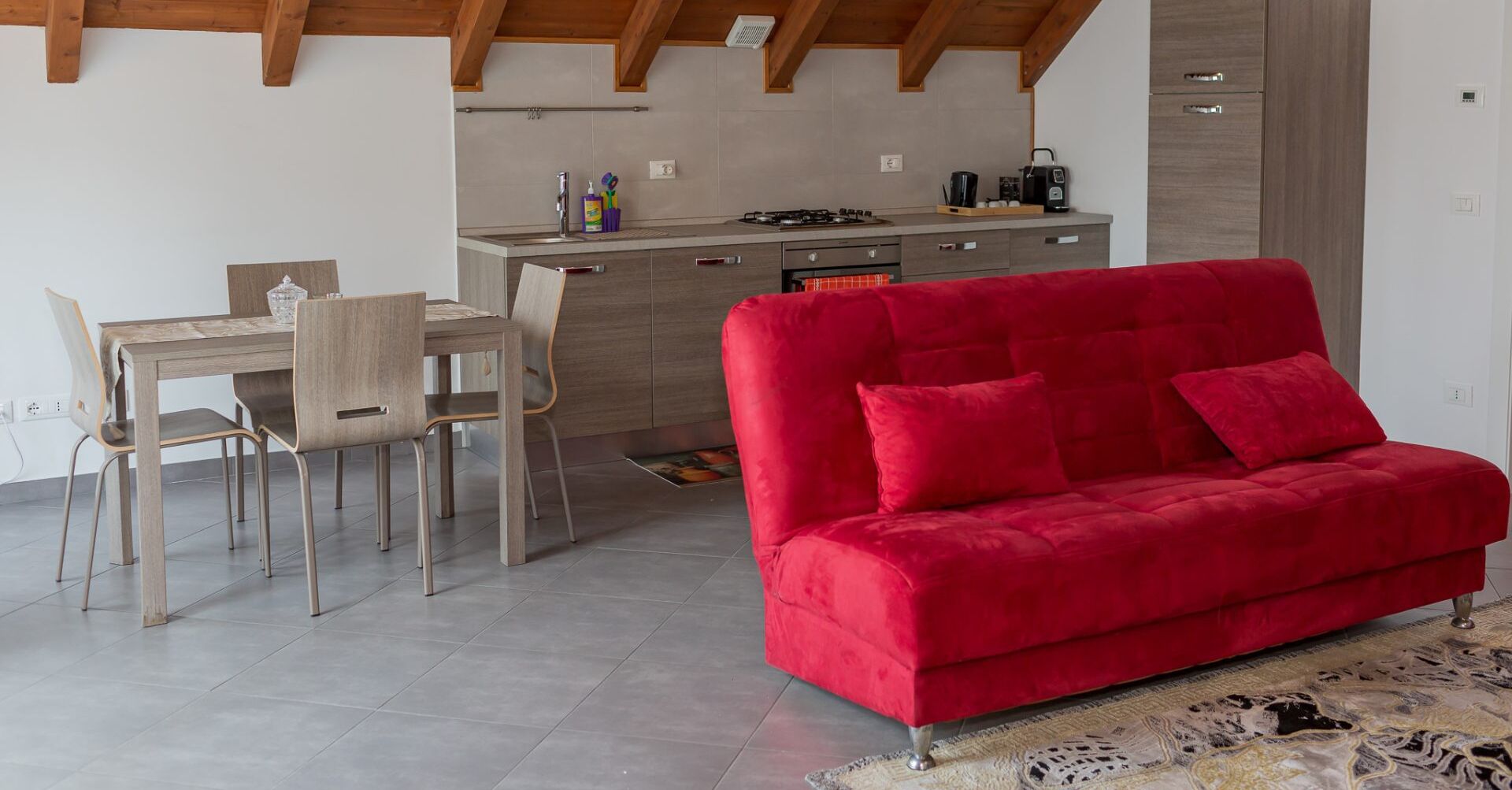 Una cucina moderna con zona pranzo, un divano rosso e un tappeto a motivi.