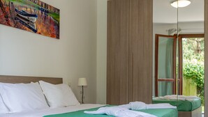 Une chambre d’hôtel avec un grand lit, une lampe de chevet et une vue sur la verdure, visible à travers une porte vitrée.