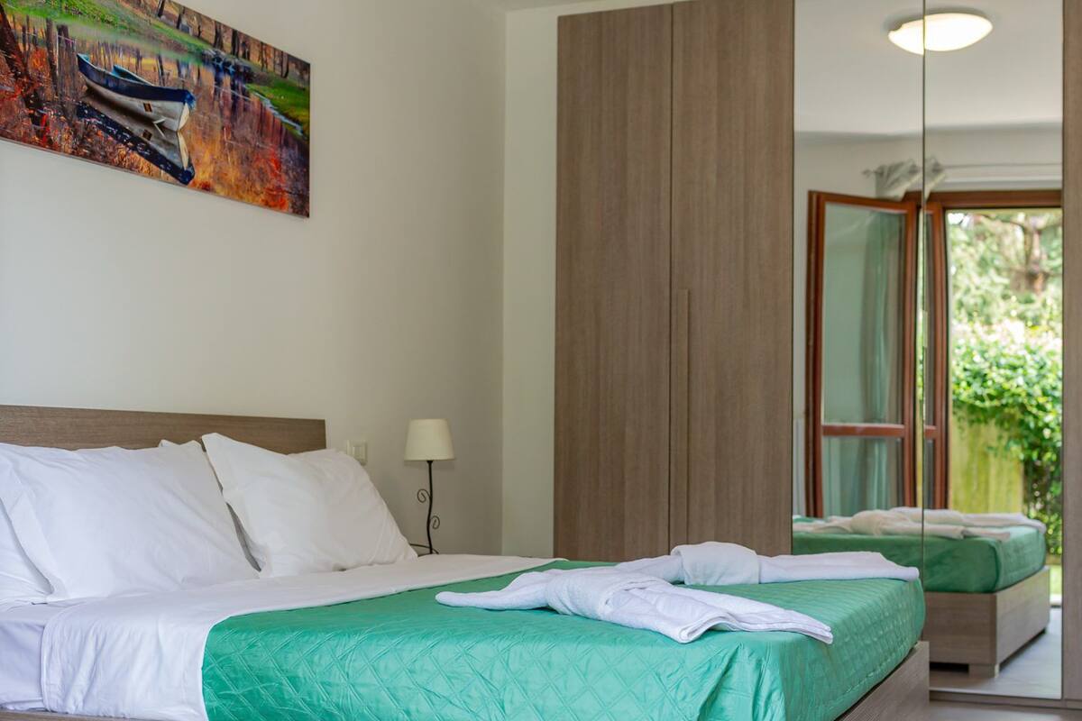 A hotel room with a large bed, a bedside lamp, and a view of greenery through a glass door.