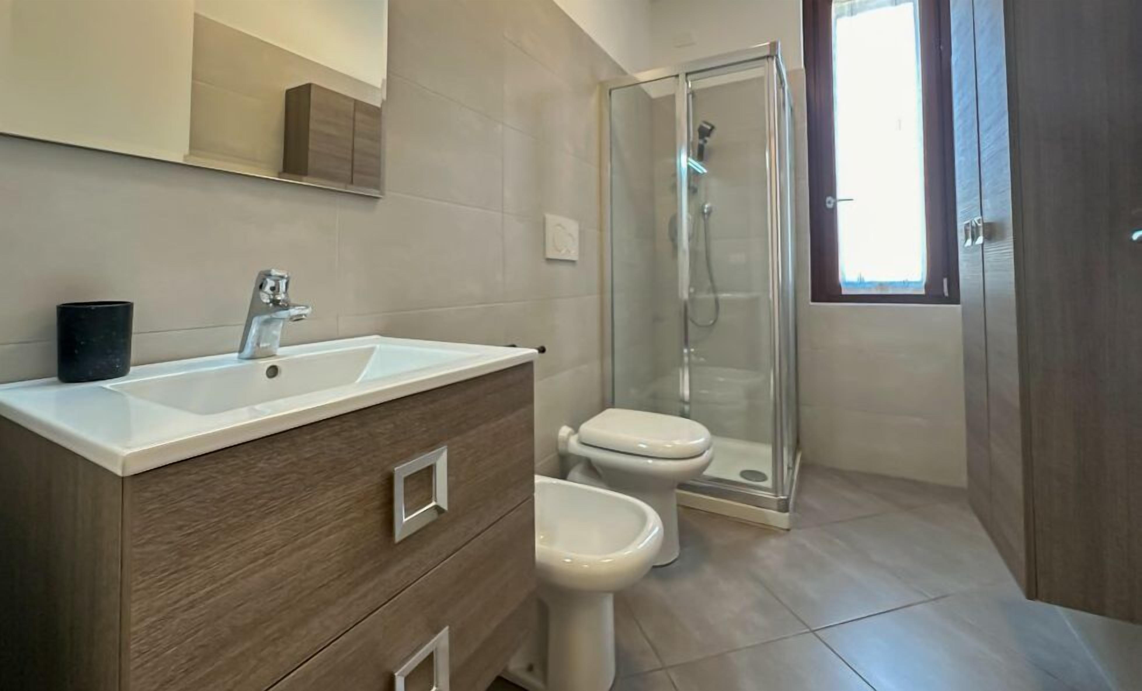 A modern bathroom with a white sink, two toilets, and a glass shower enclosure.