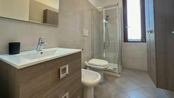 A modern bathroom with a white sink, two toilets, and a glass shower enclosure.