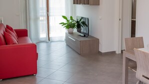 Un salon moderne avec un canapé rouge, un téléviseur posé sur un meuble en bois, une plante en pot et un coin repas avec une chaise.
