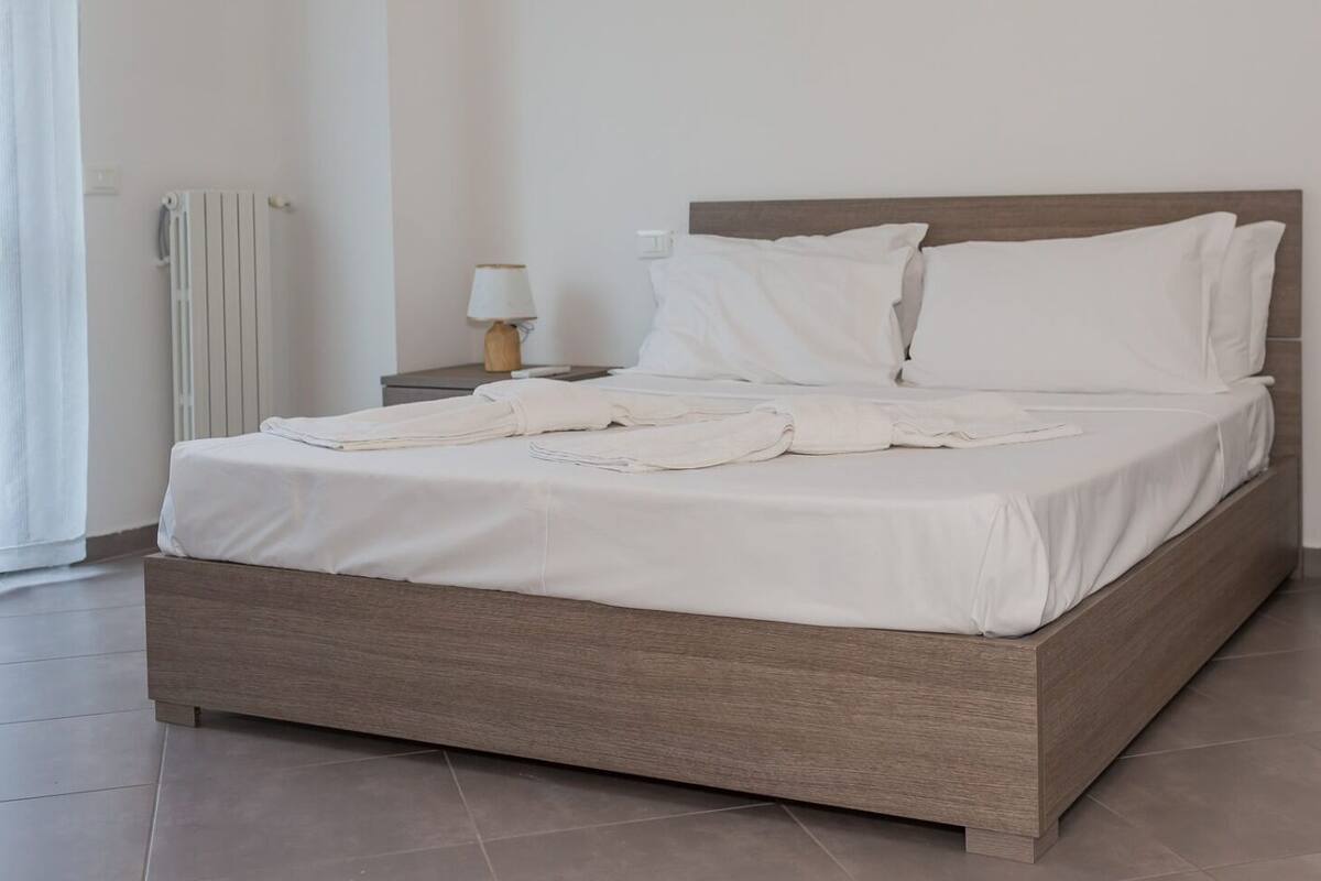 A neatly made bed with white linens, a wooden headboard, and two bedside tables with lamps.