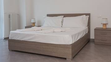 Cama bem arrumada com lençóis brancos, cabeceira de madeira e duas mesas de cabeceira com luminárias.