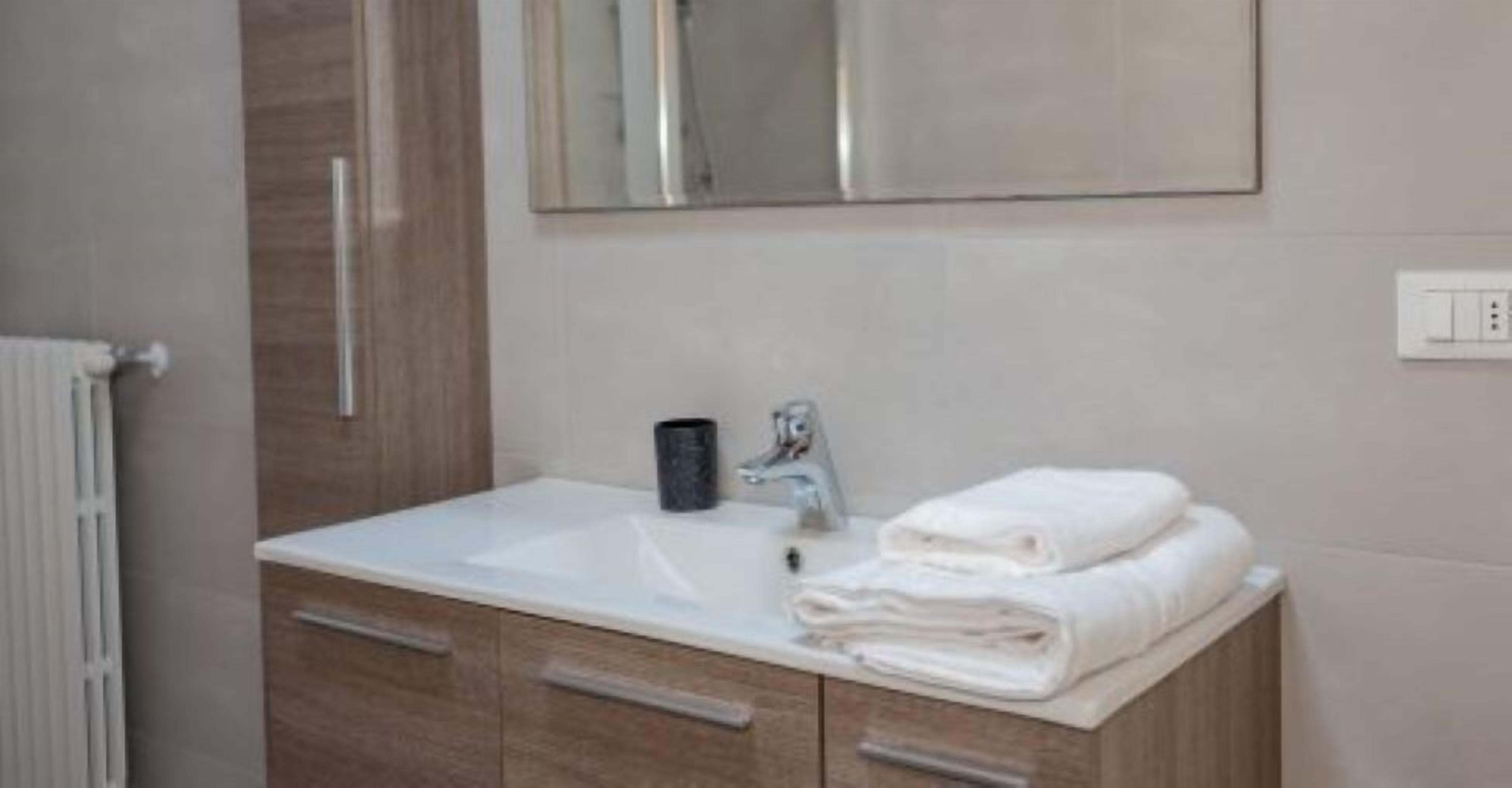 Une salle de bain avec un lavabo blanc, un miroir au-dessus et une pile de serviettes sur le comptoir.