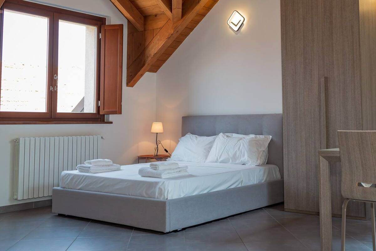 A bedroom with a bed, bedside table, lamp, and a desk with chair.