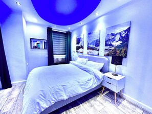 Una camera da letto moderna con un letto grande, un comodino, tende a una finestra e dipinti con paesaggi montani alle pareti.