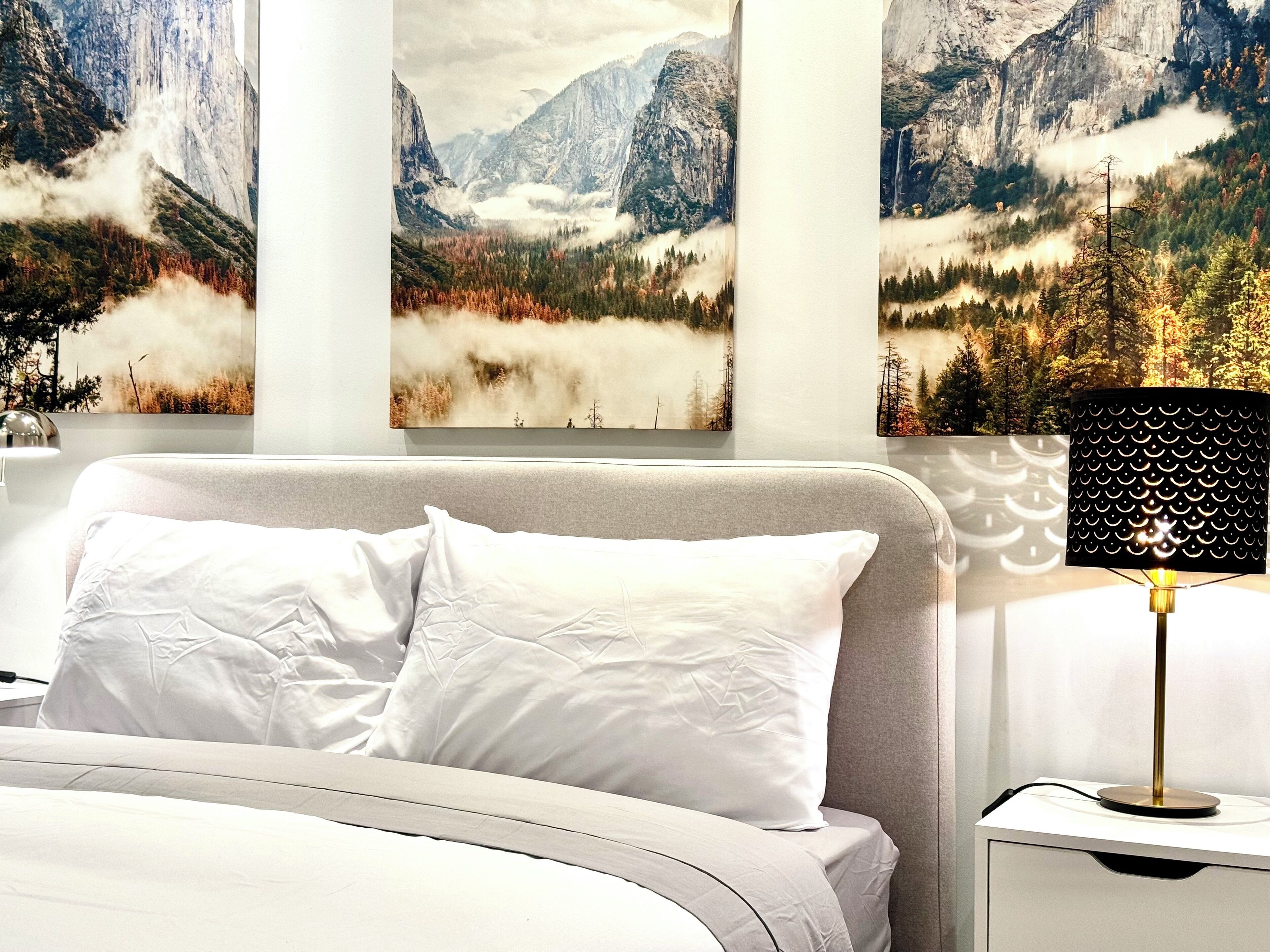A bedroom with a bed, white pillows, and a nightstand with a lamp.