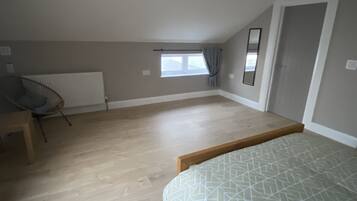 A spacious room with a sloped ceiling, a large window with curtains, a radiator, and a bed with a geometric-patterned bedspread.